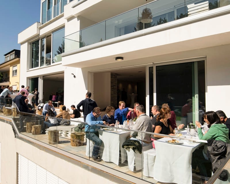 groups of people sat eating on a balcony at tables with white table covers
