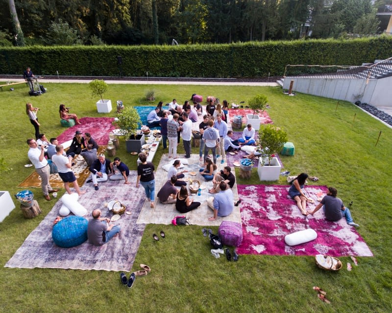 birds-eye view of people sat in a garden on the grass using picnic blankets
